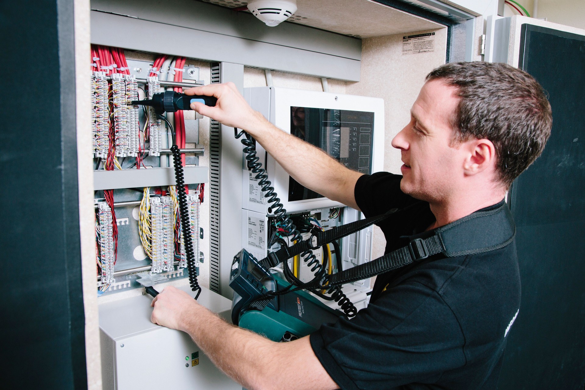 Elektrofachkraft prüft eine elektrische Steuerungsanlage mit einem Messgerät